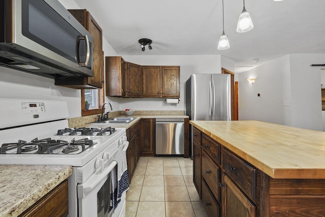 kitchen featuring dark brown cabinetry, sink, light tile patterned floors, appliances with stainless steel finishes, and pendant lighting