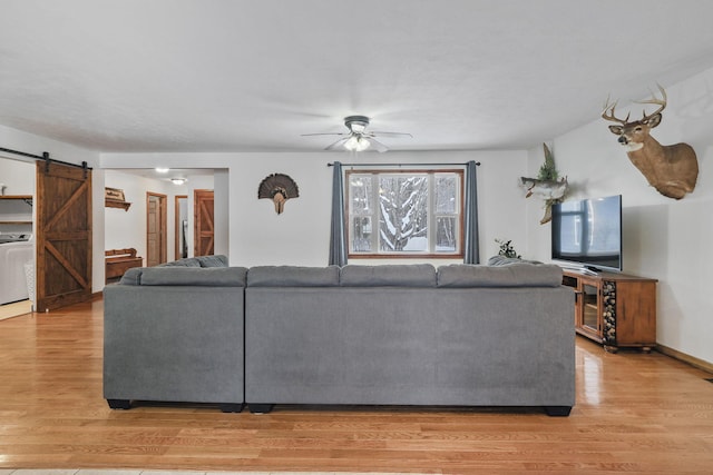 living room featuring ceiling fan, a barn door, washer / clothes dryer, and light wood-type flooring