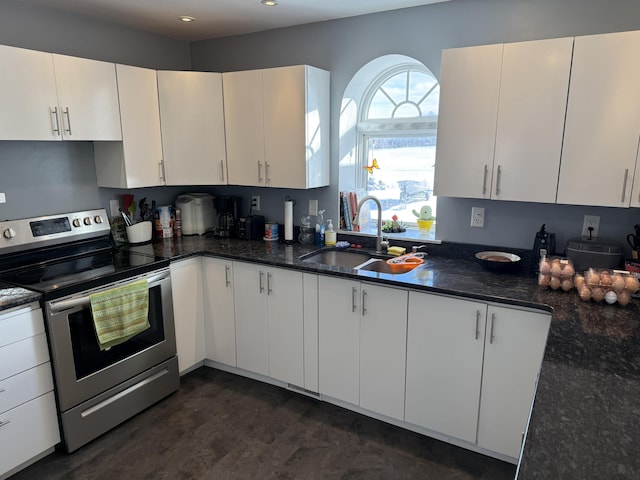 kitchen with dark stone countertops, sink, electric range, and white cabinets