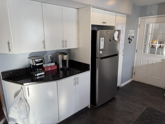 kitchen with white cabinetry, dark hardwood / wood-style floors, stainless steel refrigerator, and dark stone counters