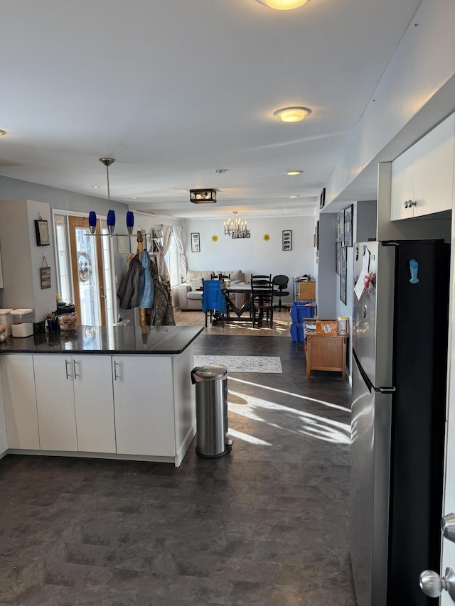 kitchen with white cabinetry, stainless steel fridge, kitchen peninsula, and hanging light fixtures