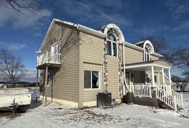 view of snowy exterior with a porch, a balcony, and central AC unit