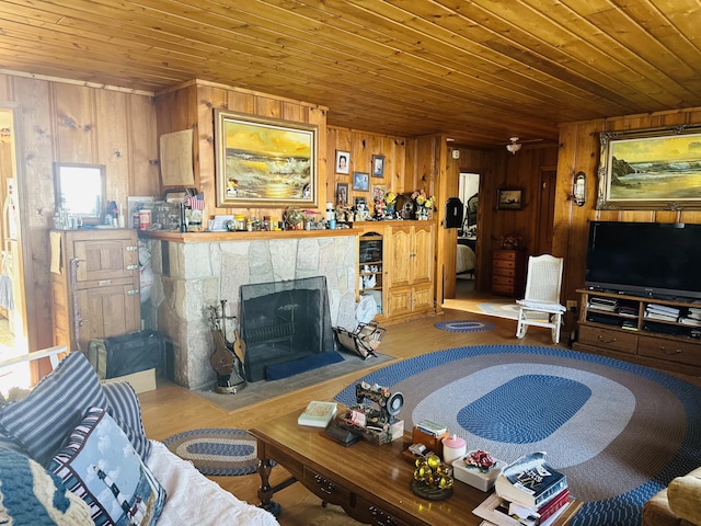 living room with a stone fireplace, wooden ceiling, and wooden walls