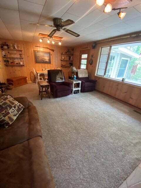 carpeted living room featuring wooden walls and ceiling fan