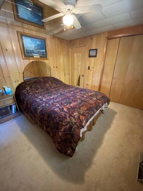 carpeted bedroom with ceiling fan and wood walls