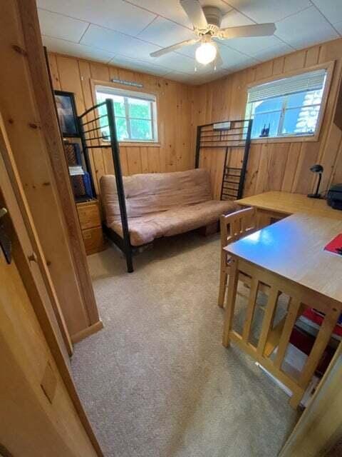 carpeted bedroom featuring wooden walls and ceiling fan