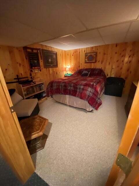 bedroom with carpet floors, a paneled ceiling, and wood walls