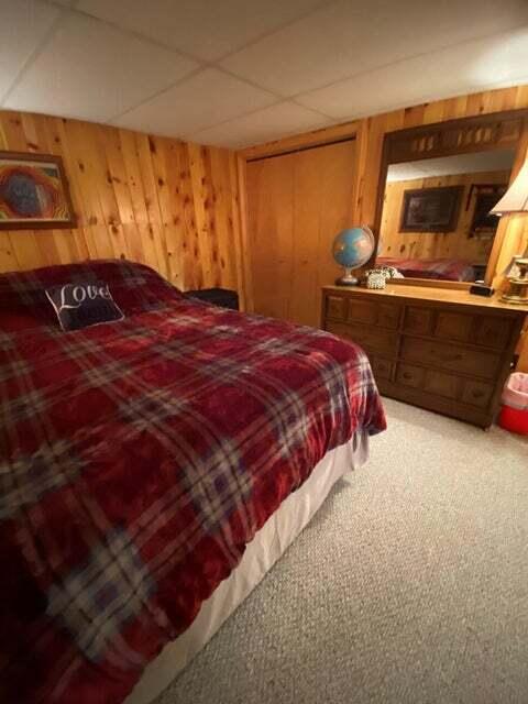 carpeted bedroom with a drop ceiling, wooden walls, and a closet