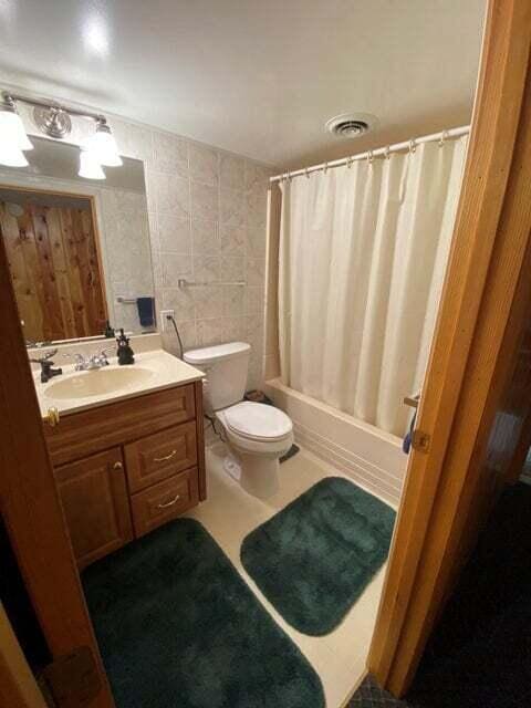 full bathroom with shower / bathtub combination with curtain, vanity, toilet, and tile walls