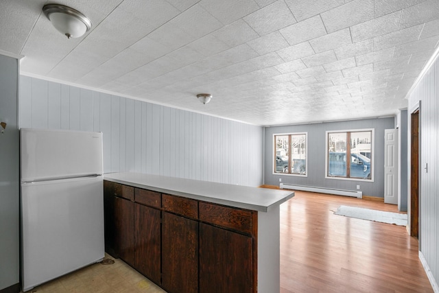 kitchen with white fridge, a baseboard heating unit, kitchen peninsula, crown molding, and dark brown cabinets