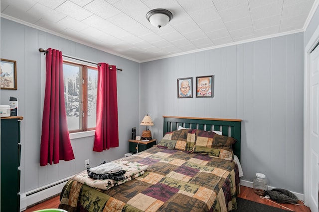 bedroom featuring ornamental molding, wood-type flooring, and a baseboard heating unit