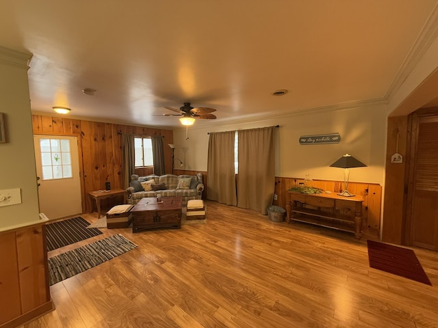 living room with ornamental molding, ceiling fan, light wood-type flooring, and wood walls