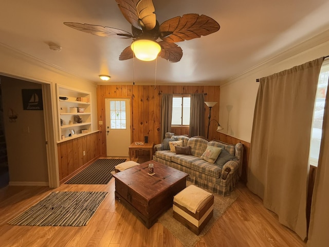 living room featuring crown molding, light hardwood / wood-style flooring, wooden walls, built in features, and ceiling fan