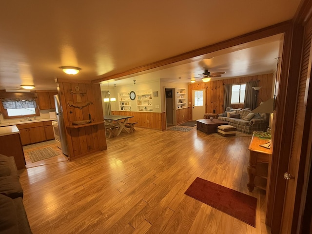 living room featuring ceiling fan, wooden walls, sink, and light hardwood / wood-style flooring