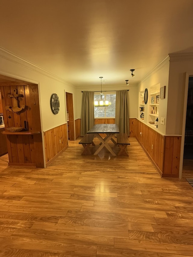 dining space featuring crown molding, a notable chandelier, light hardwood / wood-style floors, and wood walls