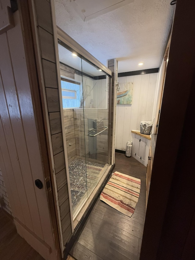 bathroom featuring hardwood / wood-style flooring, a shower with door, wooden walls, and a textured ceiling