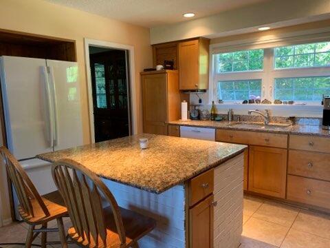 kitchen with light stone countertops, a kitchen island, a breakfast bar area, and white appliances