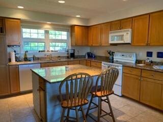 kitchen with white appliances, a kitchen bar, a kitchen island, and light tile patterned floors