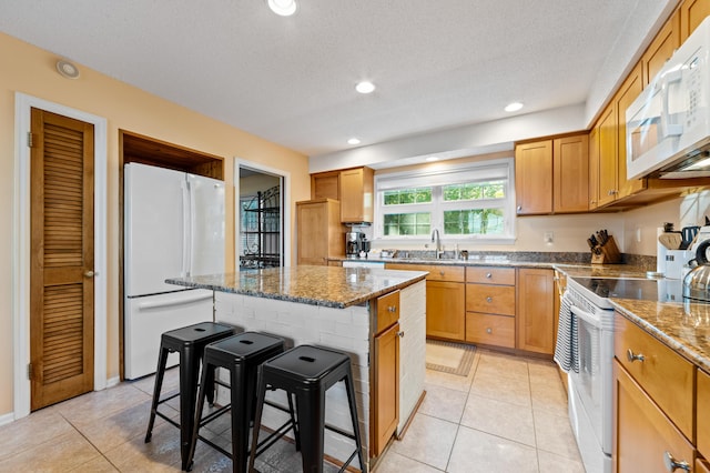 kitchen with light tile patterned flooring, a kitchen bar, sink, a kitchen island, and white appliances