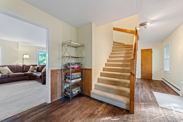 staircase featuring baseboard heating, a textured ceiling, and hardwood / wood-style flooring