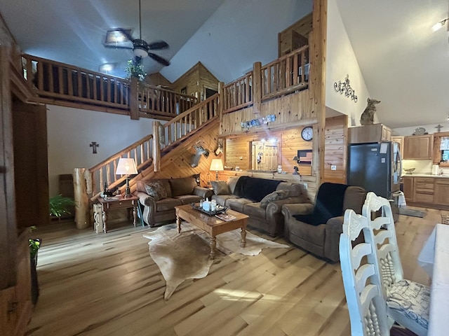 living room with ceiling fan, high vaulted ceiling, wooden walls, and light hardwood / wood-style floors