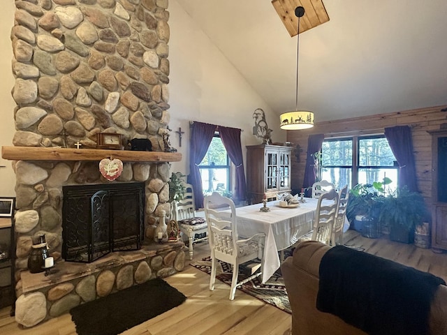 dining area featuring wood-type flooring, a stone fireplace, and high vaulted ceiling