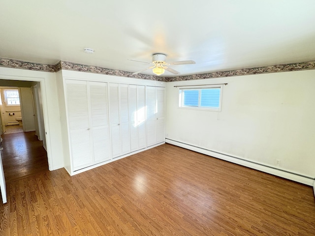 unfurnished bedroom featuring hardwood / wood-style flooring, a closet, baseboard heating, and multiple windows