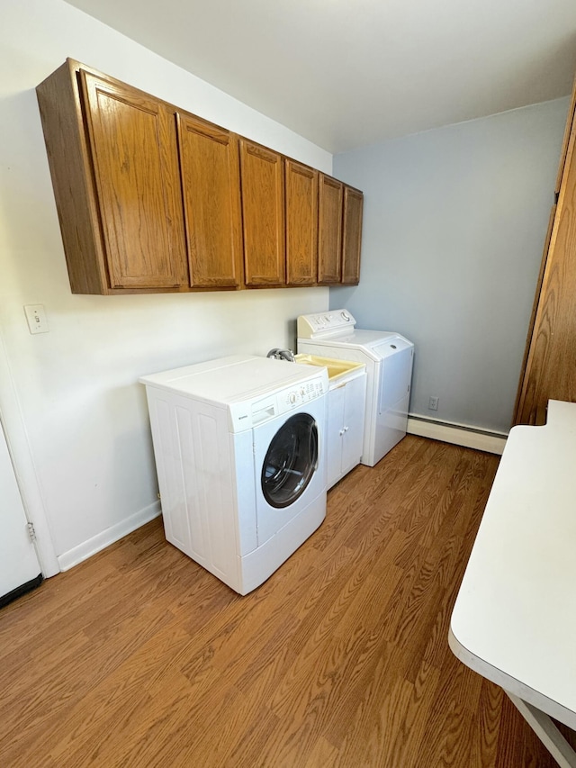 washroom featuring a baseboard radiator, light hardwood / wood-style floors, cabinets, and washing machine and clothes dryer