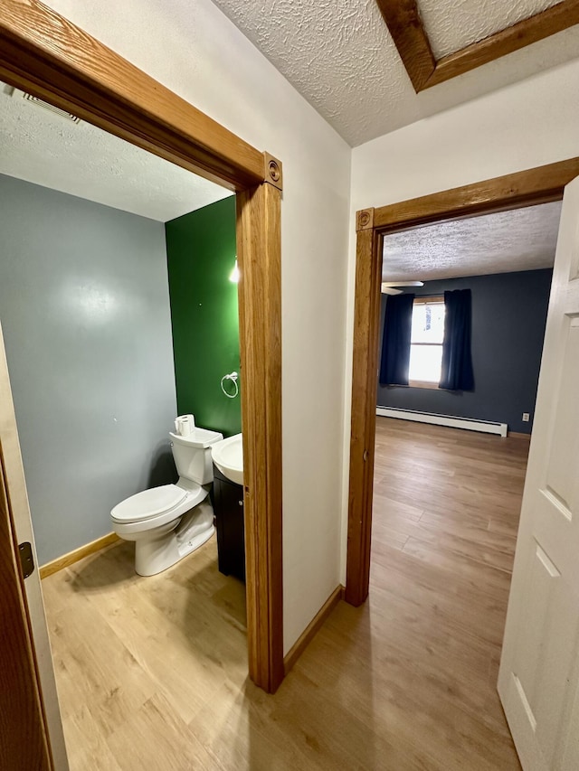 bathroom with baseboard heating, toilet, a textured ceiling, and hardwood / wood-style flooring