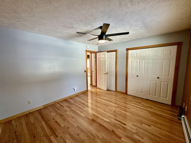 unfurnished bedroom with a textured ceiling, a baseboard radiator, light hardwood / wood-style floors, and multiple closets