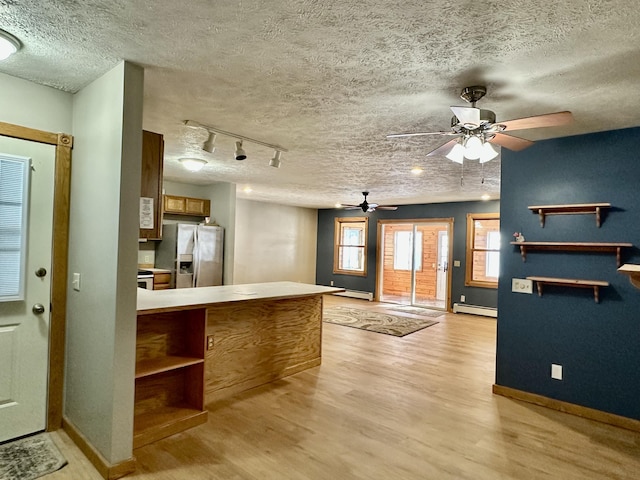 kitchen with a textured ceiling, a baseboard radiator, stainless steel fridge, kitchen peninsula, and light hardwood / wood-style floors