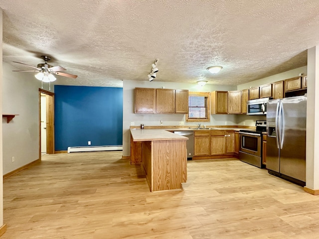 kitchen with light hardwood / wood-style flooring, baseboard heating, appliances with stainless steel finishes, a center island, and a textured ceiling