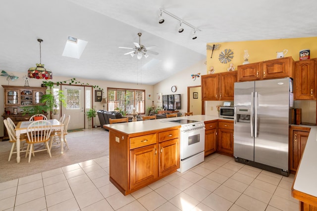 kitchen with lofted ceiling with skylight, stainless steel appliances, kitchen peninsula, and light tile patterned flooring