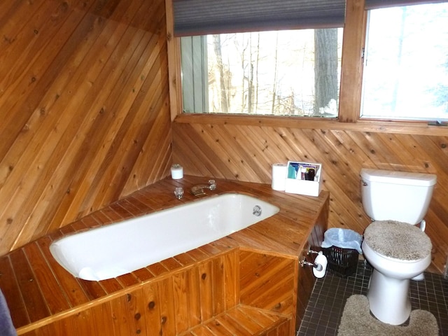 bathroom featuring wooden walls, toilet, a bathing tub, and tile patterned flooring