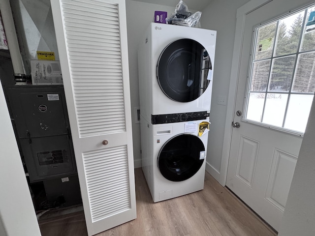 laundry area featuring a wealth of natural light, light hardwood / wood-style flooring, and stacked washing maching and dryer