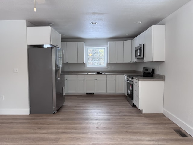 kitchen with stainless steel appliances, white cabinetry, and light wood-type flooring