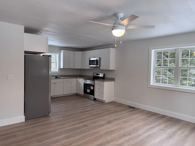 kitchen with a textured ceiling, light wood-type flooring, ceiling fan, stainless steel appliances, and white cabinets