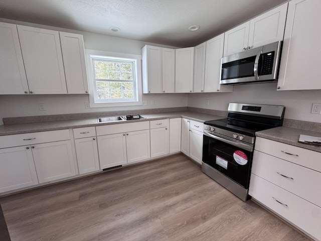 kitchen featuring sink, white cabinetry, a textured ceiling, light wood-type flooring, and stainless steel appliances