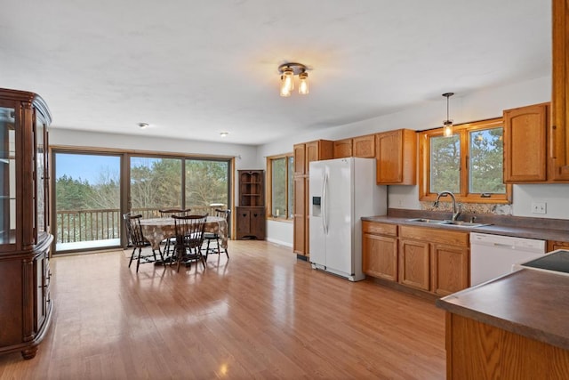 kitchen featuring hanging light fixtures, white appliances, sink, and light wood-type flooring