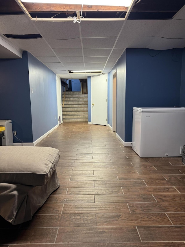 basement with hardwood / wood-style floors, a paneled ceiling, and refrigerator