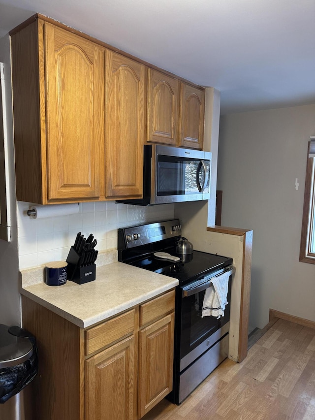 kitchen with stainless steel appliances, backsplash, and light hardwood / wood-style flooring