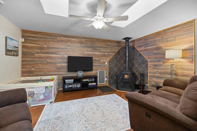 living room featuring ceiling fan, wood walls, hardwood / wood-style floors, and a wood stove