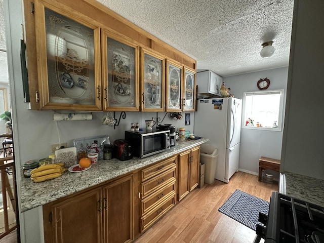 kitchen featuring white fridge, a textured ceiling, light stone counters, and light hardwood / wood-style flooring