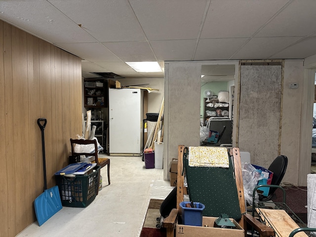 basement with white refrigerator, a paneled ceiling, and wooden walls