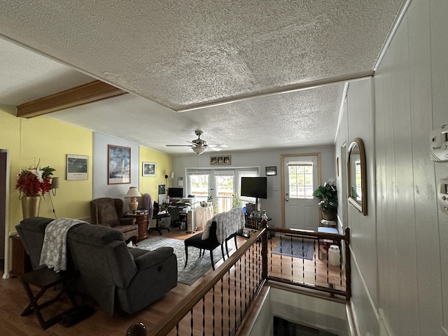 living room with beamed ceiling, wood-type flooring, ceiling fan, and a textured ceiling