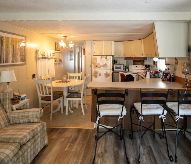 kitchen with a chandelier, a kitchen breakfast bar, dark hardwood / wood-style floors, kitchen peninsula, and white appliances