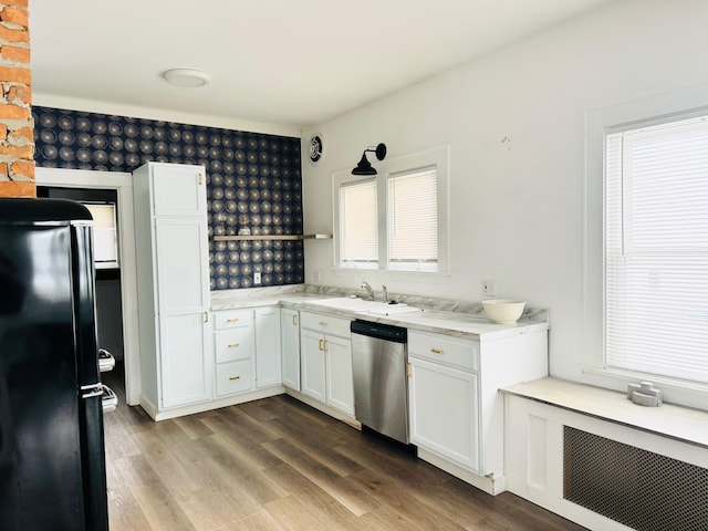 kitchen with black refrigerator, white cabinetry, sink, stainless steel dishwasher, and light hardwood / wood-style flooring