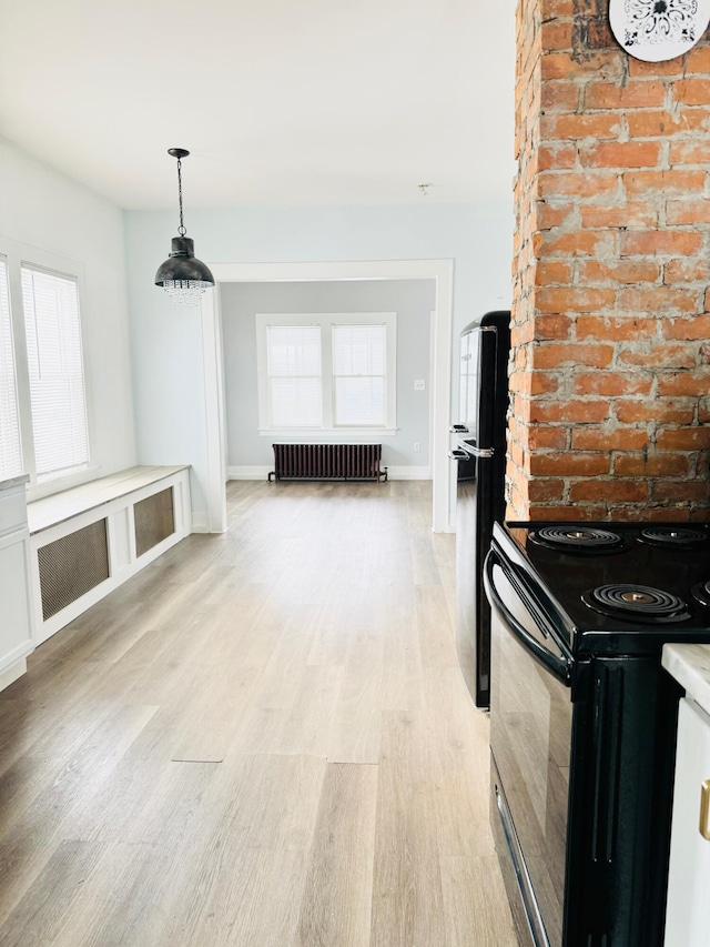 kitchen with radiator, light wood-type flooring, hanging light fixtures, and black appliances