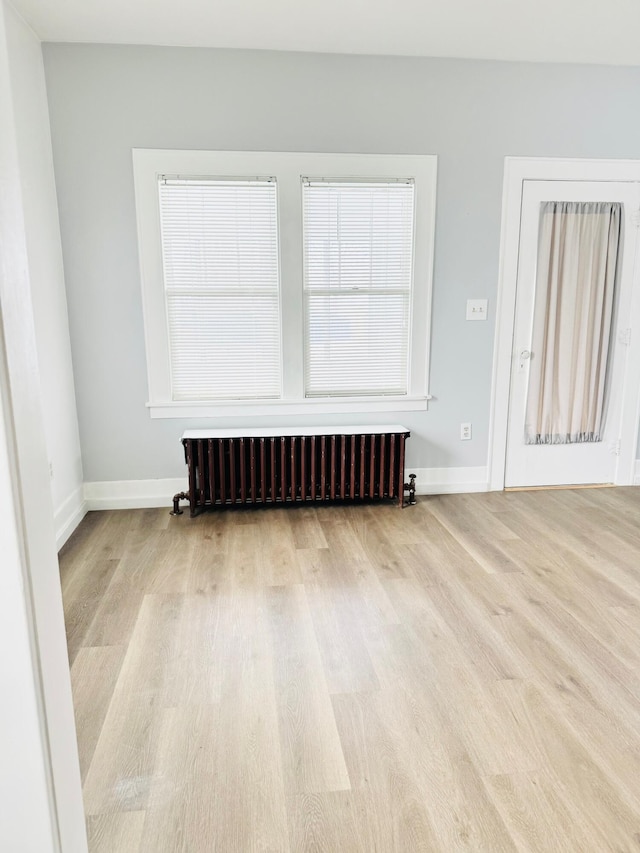 spare room with radiator heating unit and light hardwood / wood-style floors