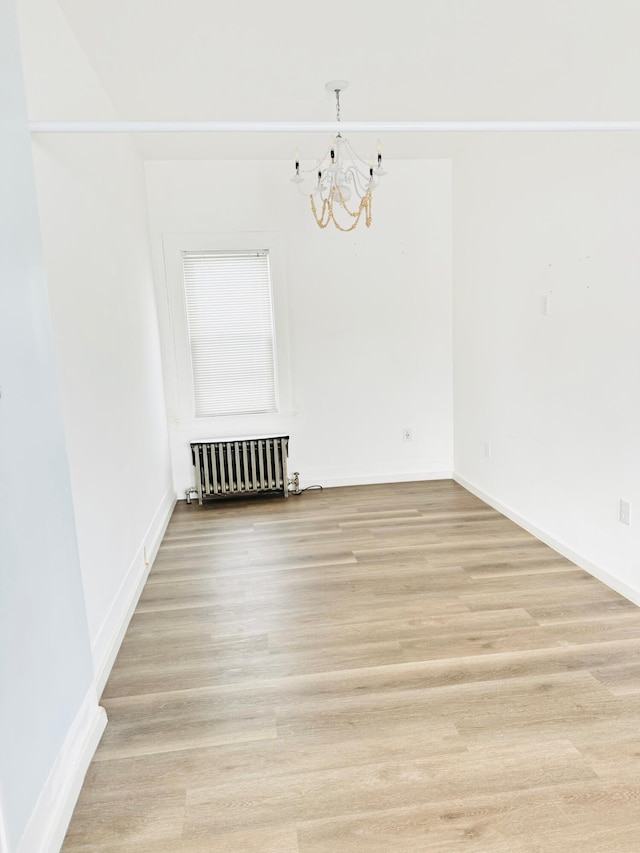 unfurnished dining area with an inviting chandelier, radiator heating unit, and light hardwood / wood-style floors